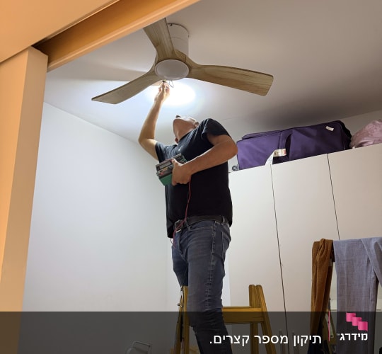 אדם מתקין מאוורר תקרה בחדר על סולם